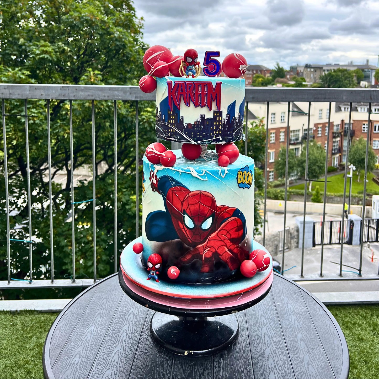 2 step Spider-Man birthday cake on a table with a cityscape background
