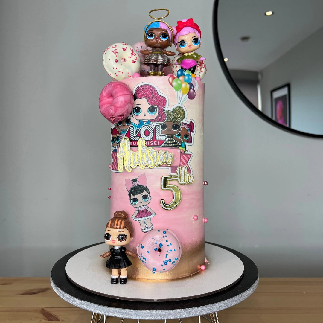 A LOL SURPRISE DOLLS themed buttercream cake designed with colorful cartoon characters, donuts, and sprinkles on top, placed on a round cake stand.
