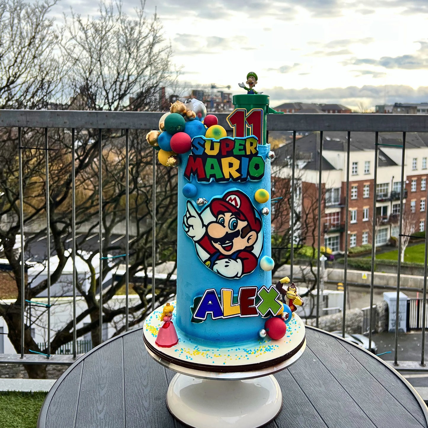 Super Mario birthday cake with colorful decorations on a table outdoors.