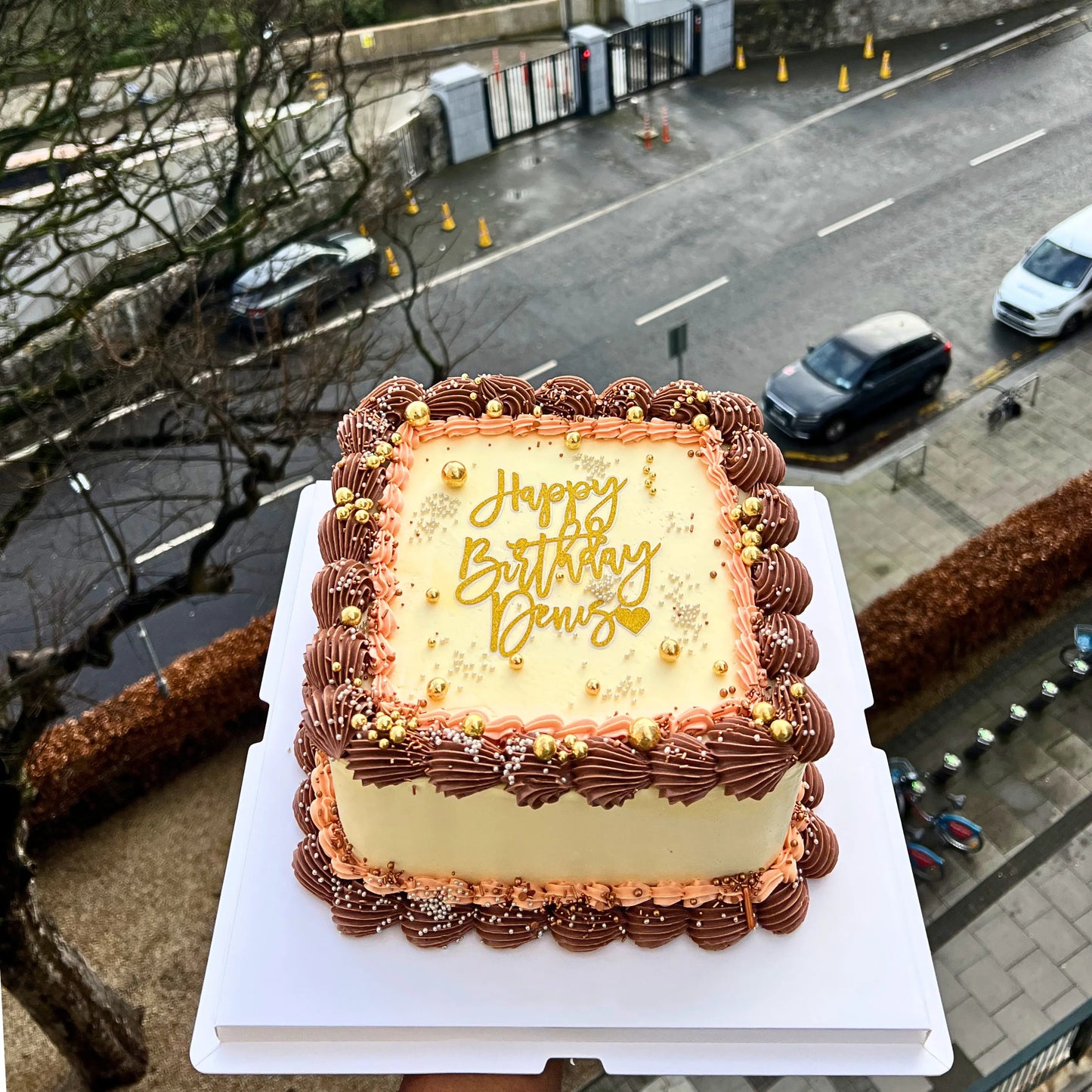 Rectangular birthday cake with 'Happy Birthday Denis' on a street background