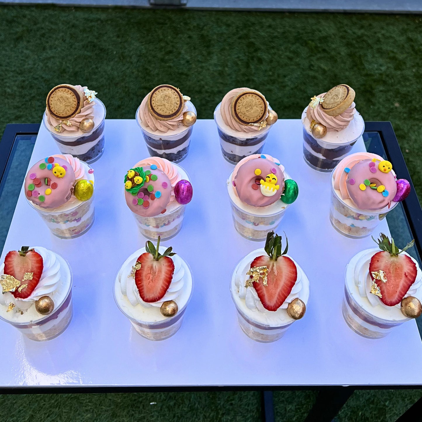 Assorted small cheeses cake shooters desserts on a white tray with a grassy background
