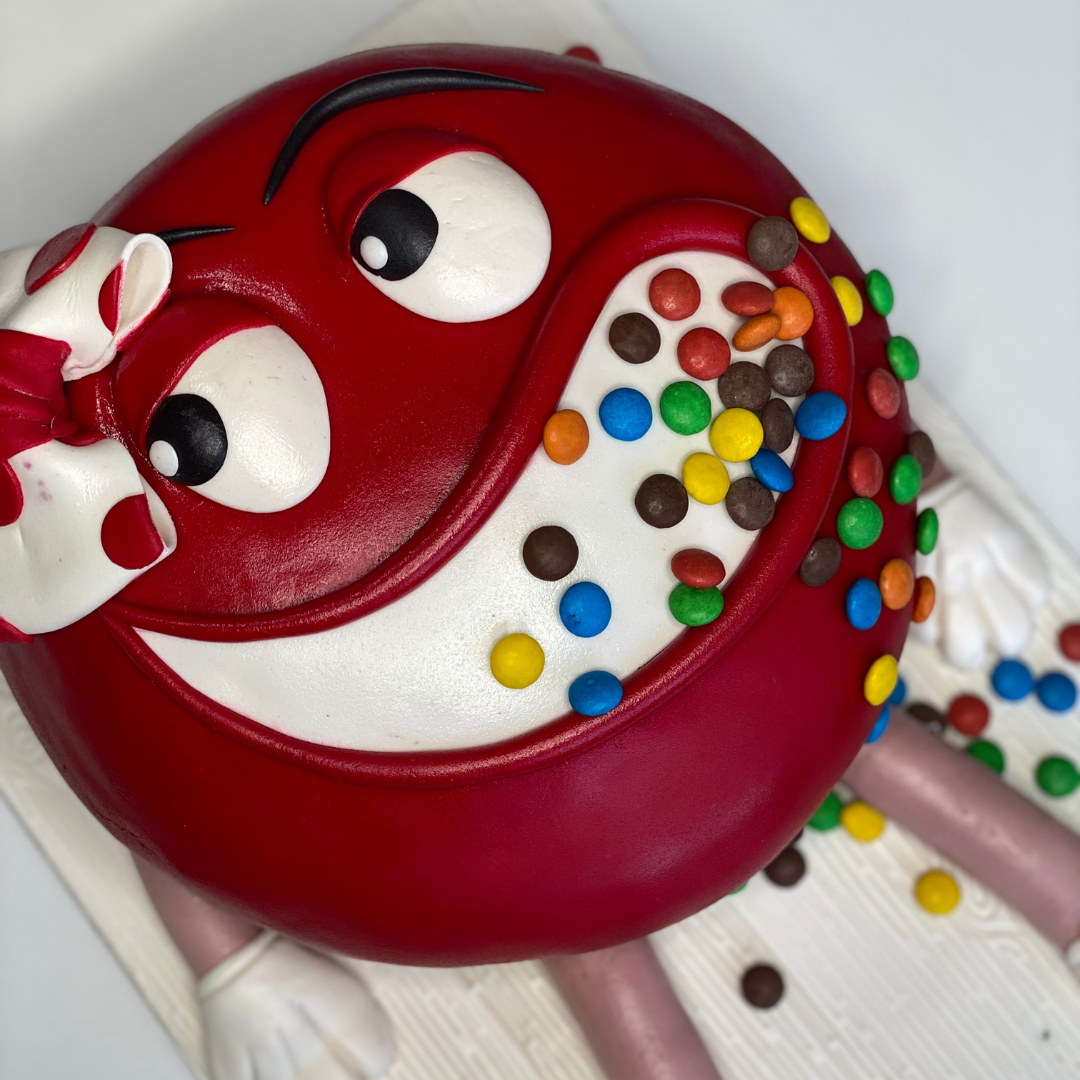 A custom M&M cake designed with a red and white character decoration, topped with colorful M&M candies.