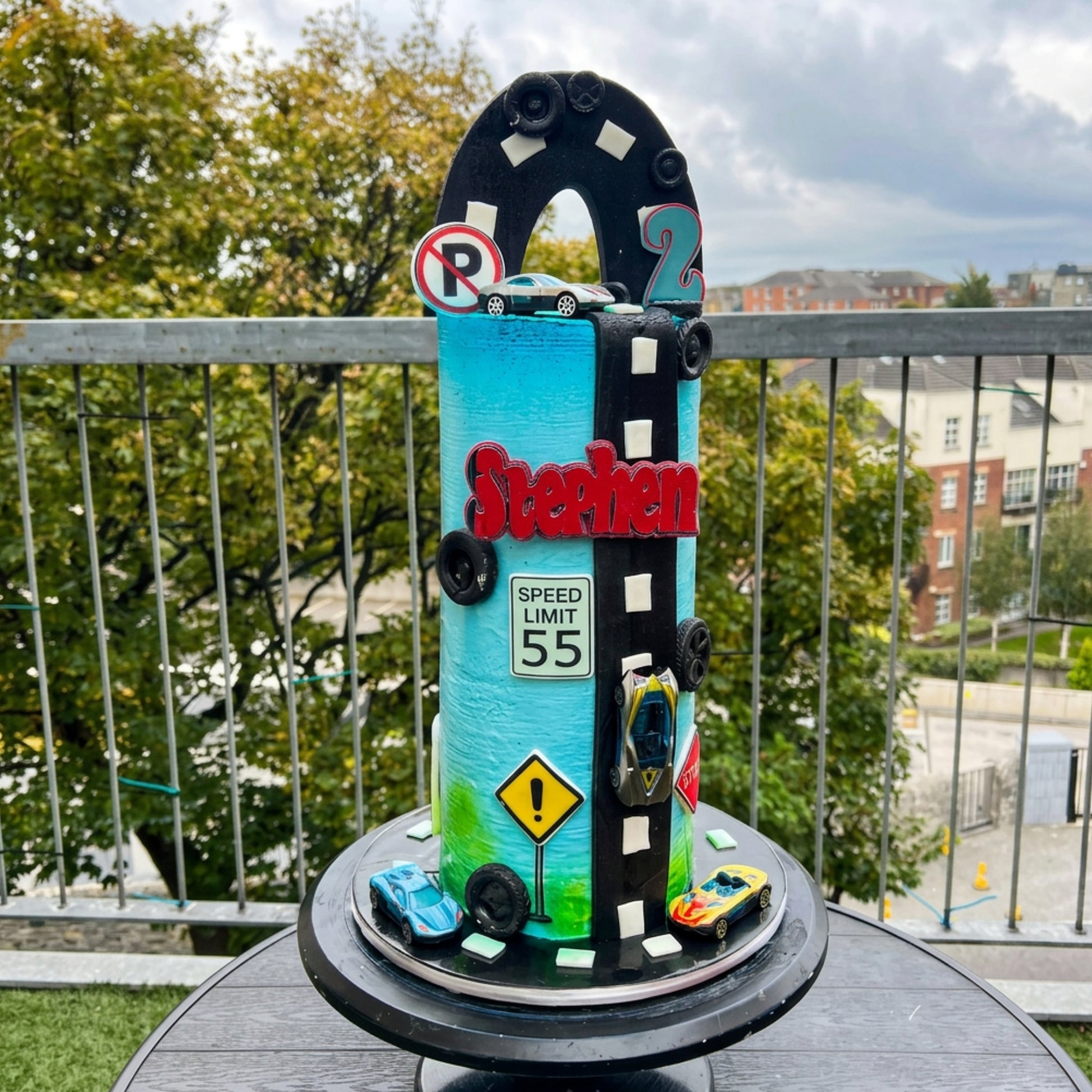 Tall turquoise race car birthday cake with fondant racetrack, speed limit sign and toy cars, handmade in Dublin by CakeMeAway