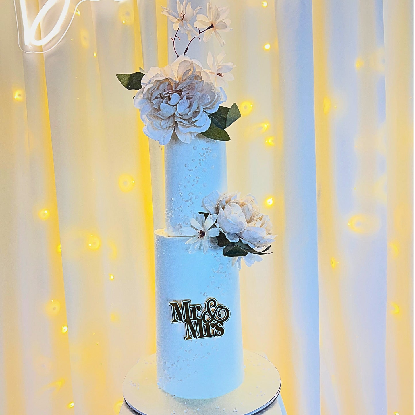 Pearl wedding cake with peonies and magnolia blossom against a lit backdrop, CakeMeAway Dublin
