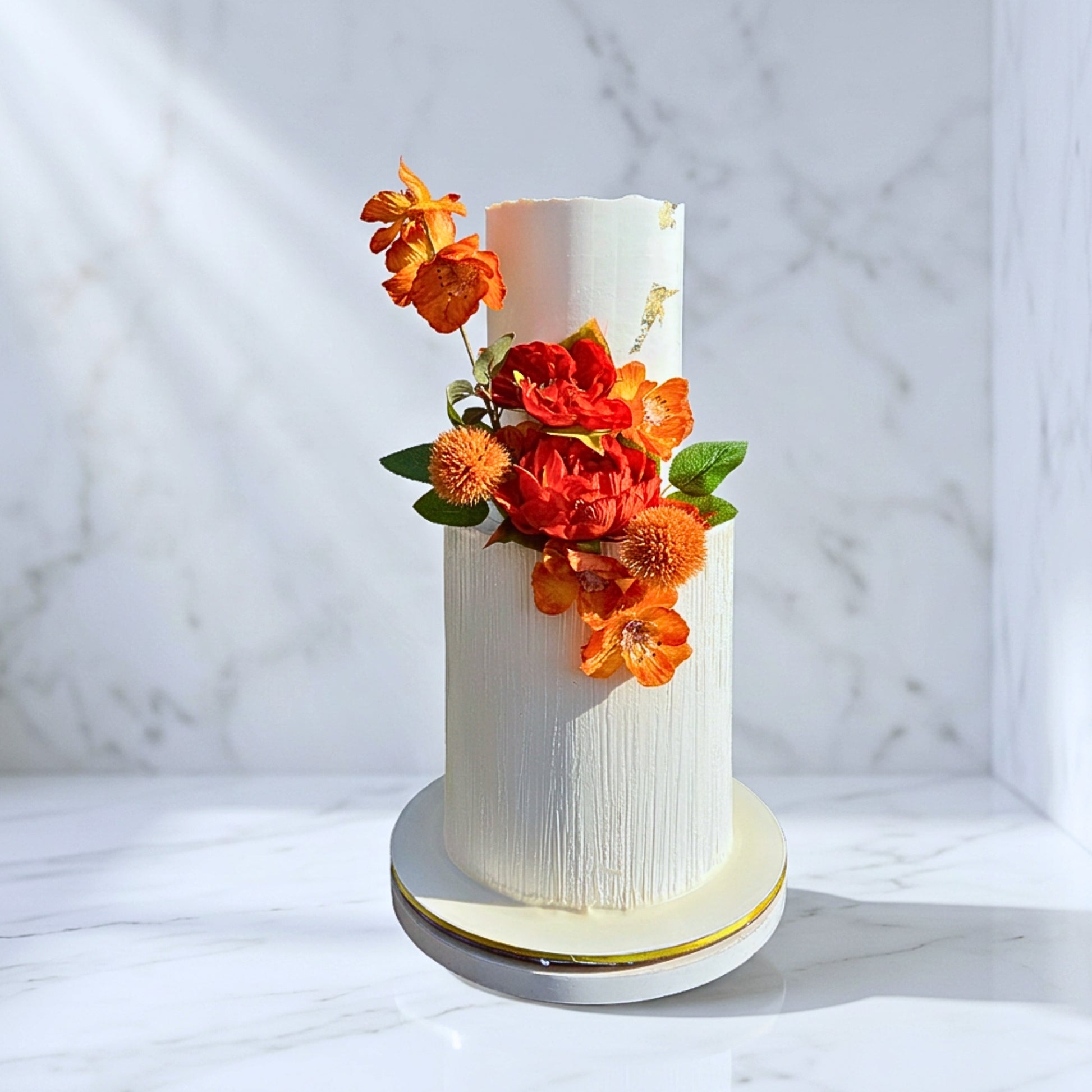 Two tier ivory wedding cake with combed buttercream texture, gold leaf and bold rust and orange florals, handmade in Dublin by CakeMeAway