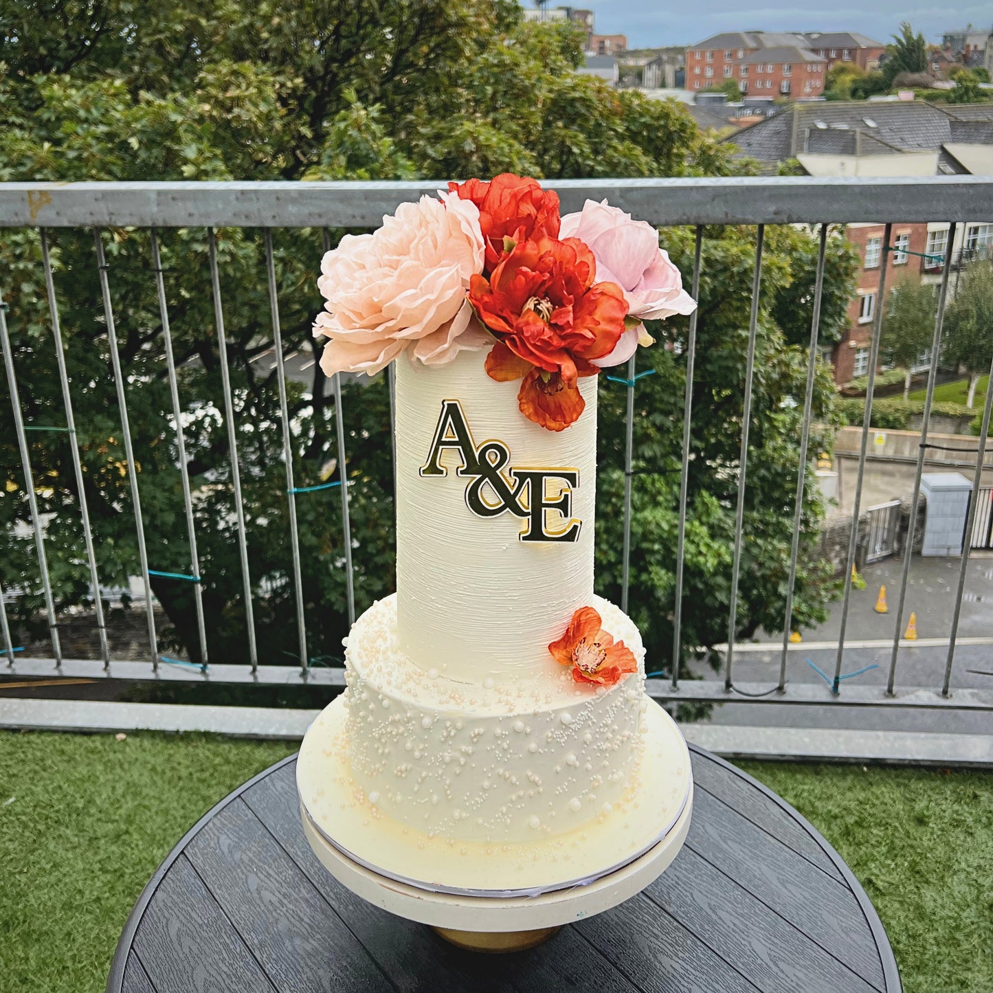 Combed buttercream wedding cake with gold monogram and autumn florals on a balcony in Dublin