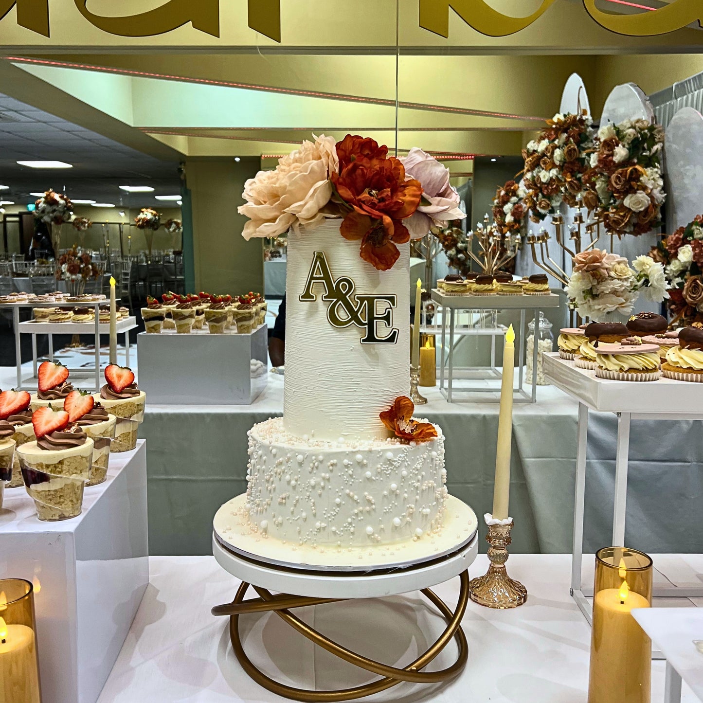 Monogram wedding cake with gold initials on a dessert table with cupcakes and candles, CakeMeAway Dublin