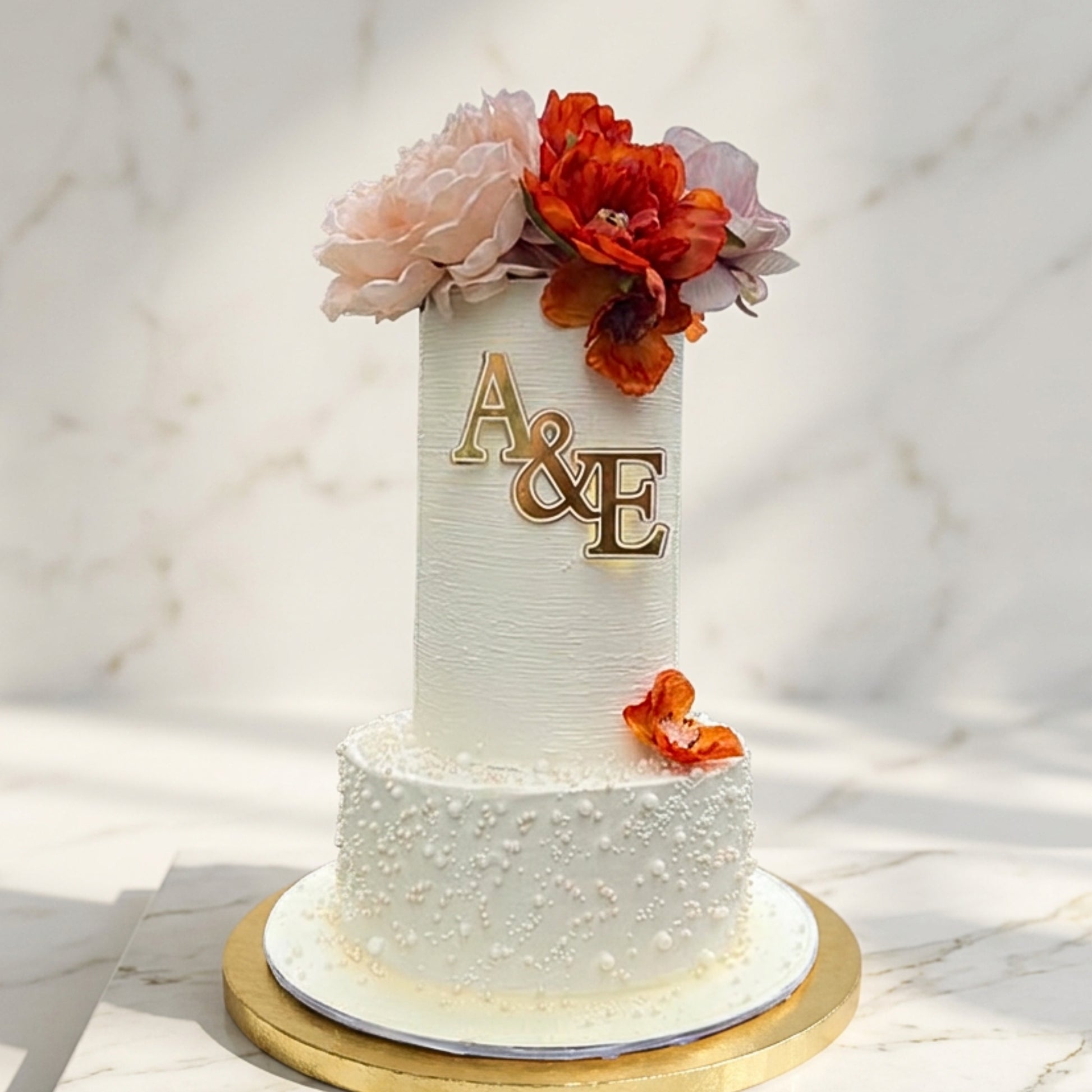 Two tier ivory monogram wedding cake with gold initials, sugar pearls and rust and blush florals, handmade in Dublin by CakeMeAway