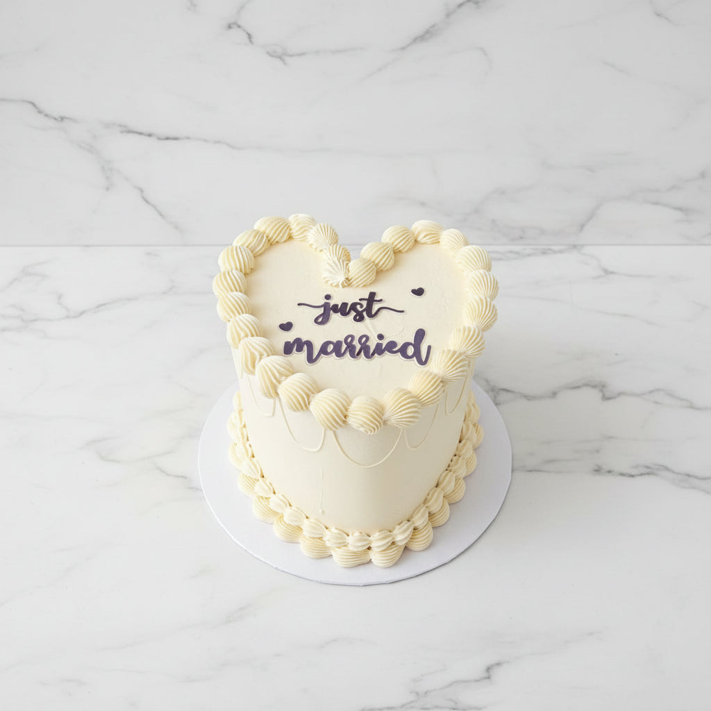 Heart-shaped cake with 'just married' text on a wooden table outdoors.