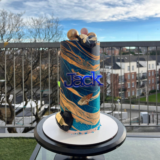 A split-design birthday cake featuring a blue superhero theme on one side and a pink floral theme on the other.