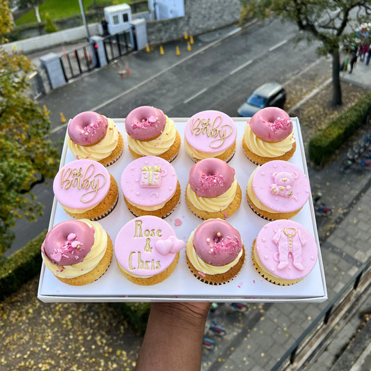 Box of pink and yellow baby shower cupcakes with personalized messages held above a street.