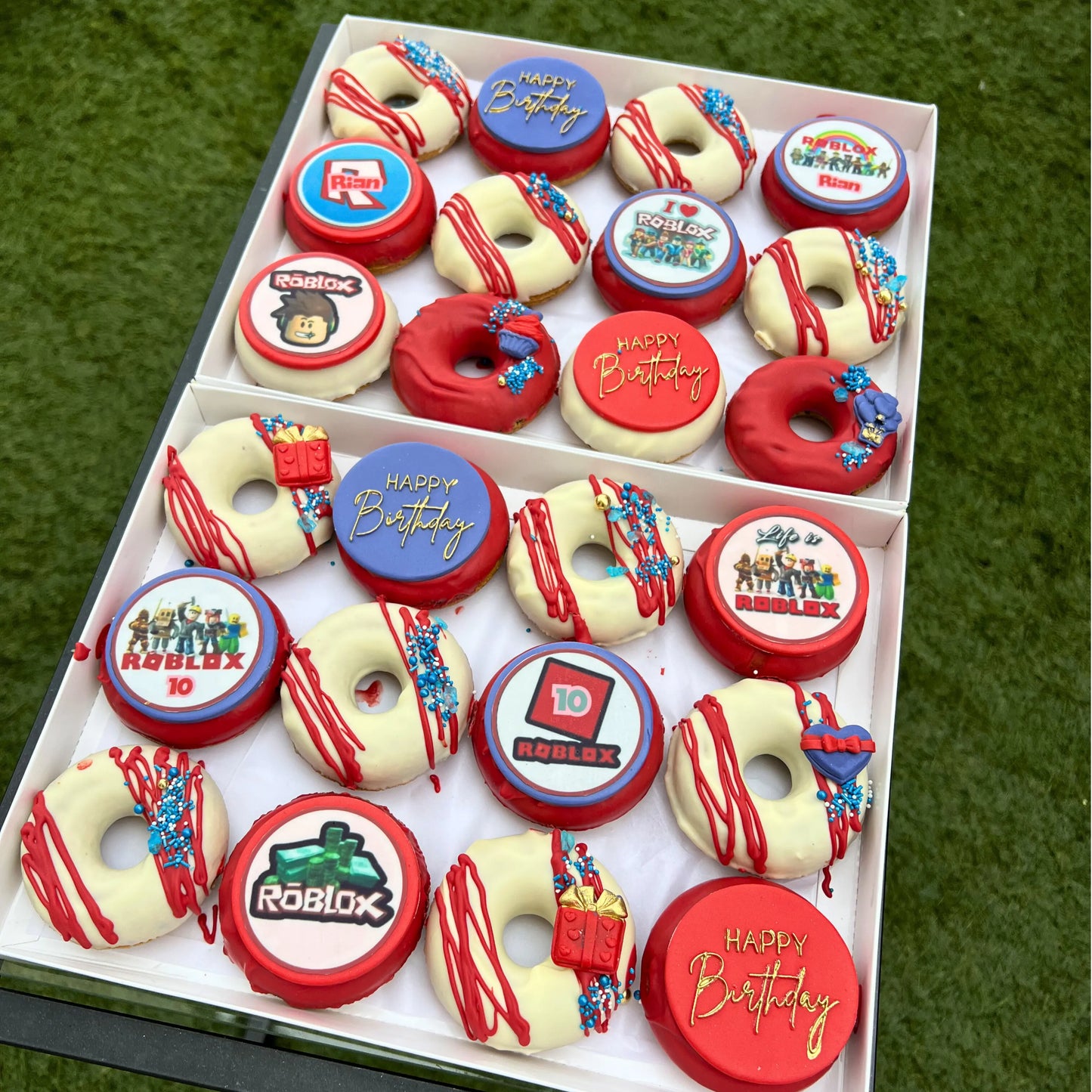 Box of themed birthday baked doughnuts with various designs and text on a green grass background