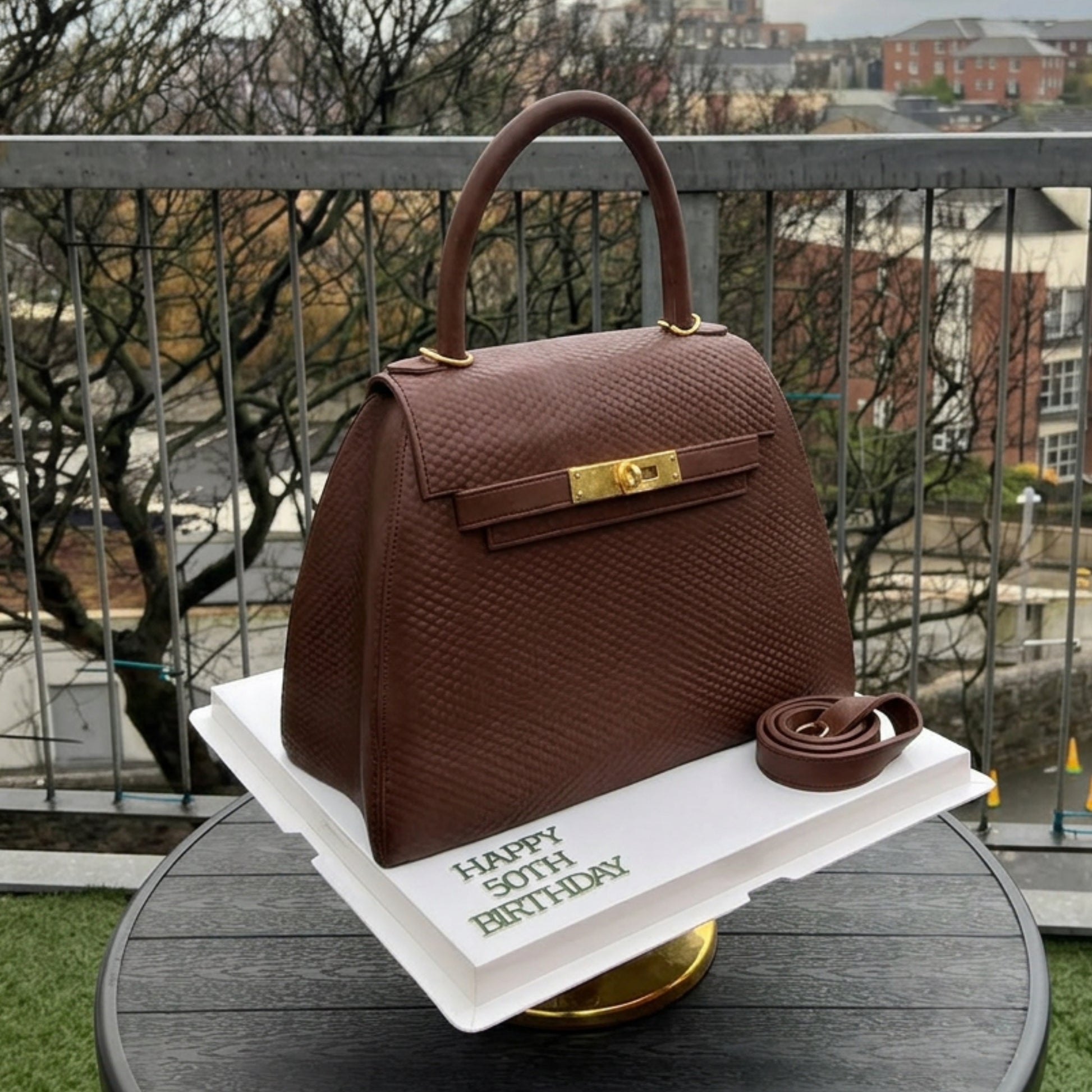 Brown structured handbag cake with a gold turn-lock and single top handle