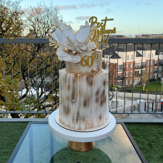 A decorated buttercream cake with wafer wraps and golden accents on a stand, displaying '60th' and 'Mr & Mrs' on top.