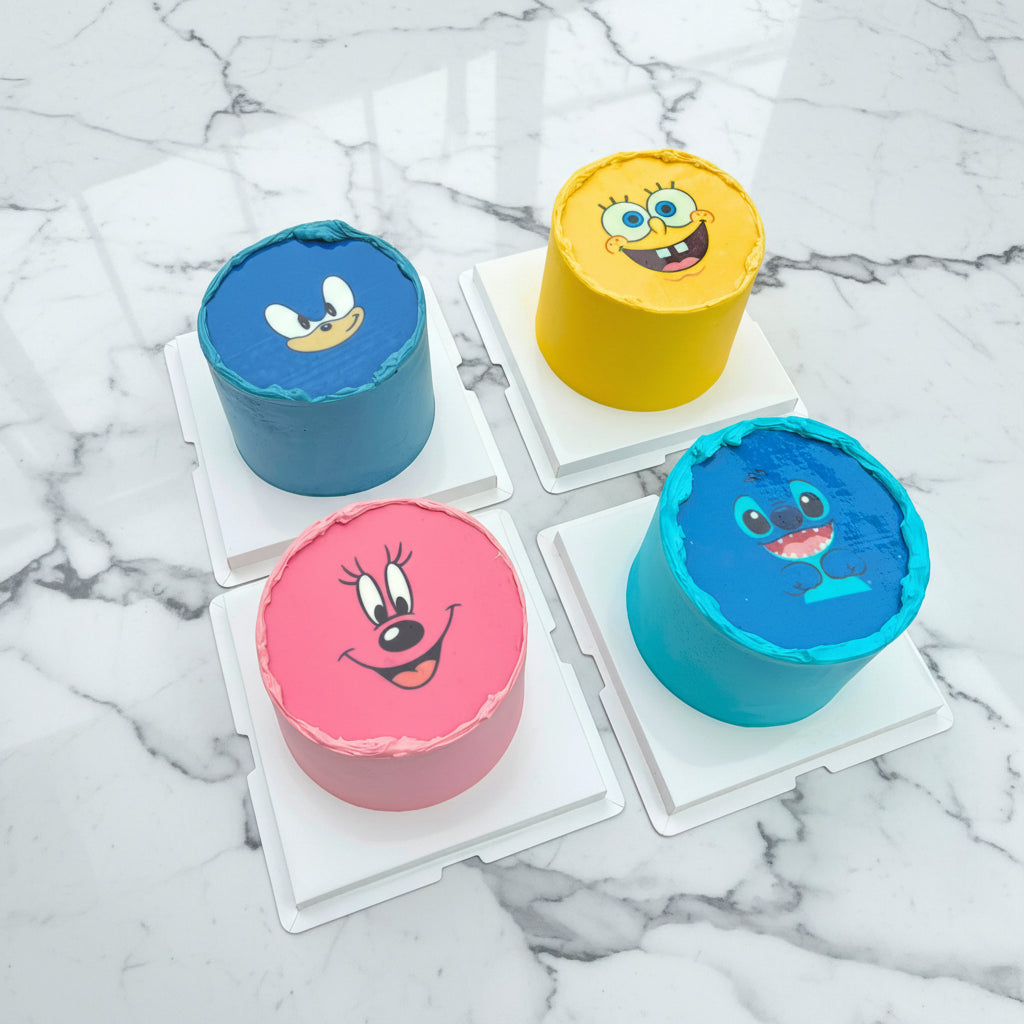 Four small cakes with cartoon character faces on a white surface.
