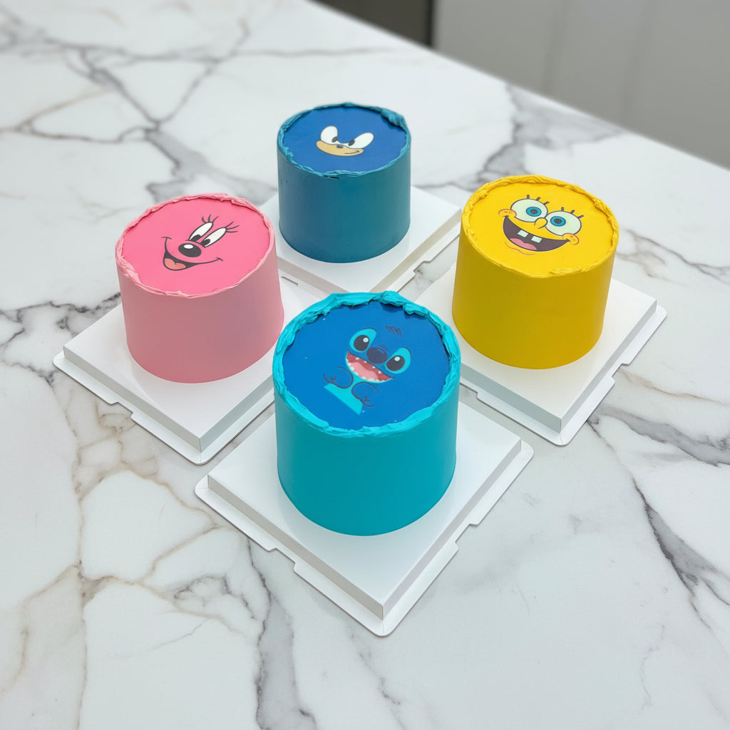 Four small cakes with cartoon character faces on a white surface.