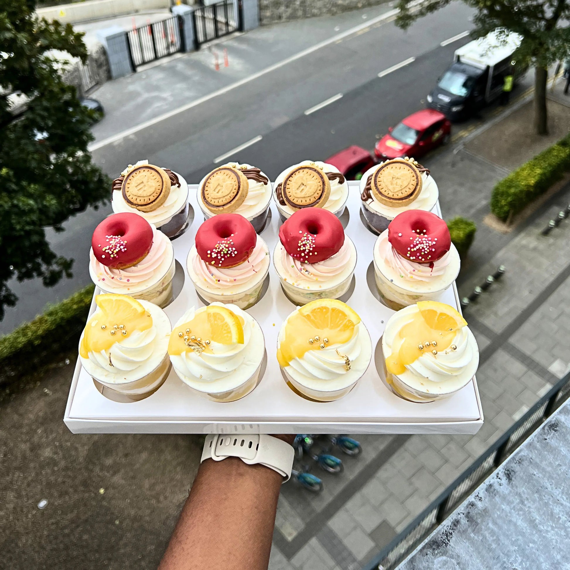 Tray of small Cheesecake  desserts held by a person with a city street in the background