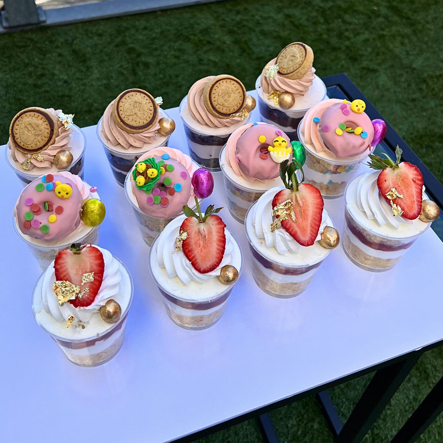 Assorted decorated cheese cake cups on a white surface with a grassy background