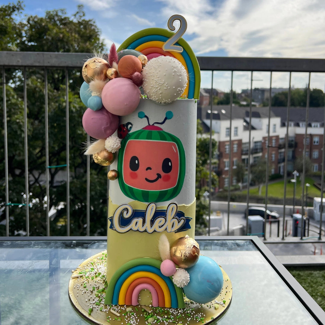A decorated cake with colorful balloons and a character from Cocomelon theme, with the name 'Caleb' displayed on it.