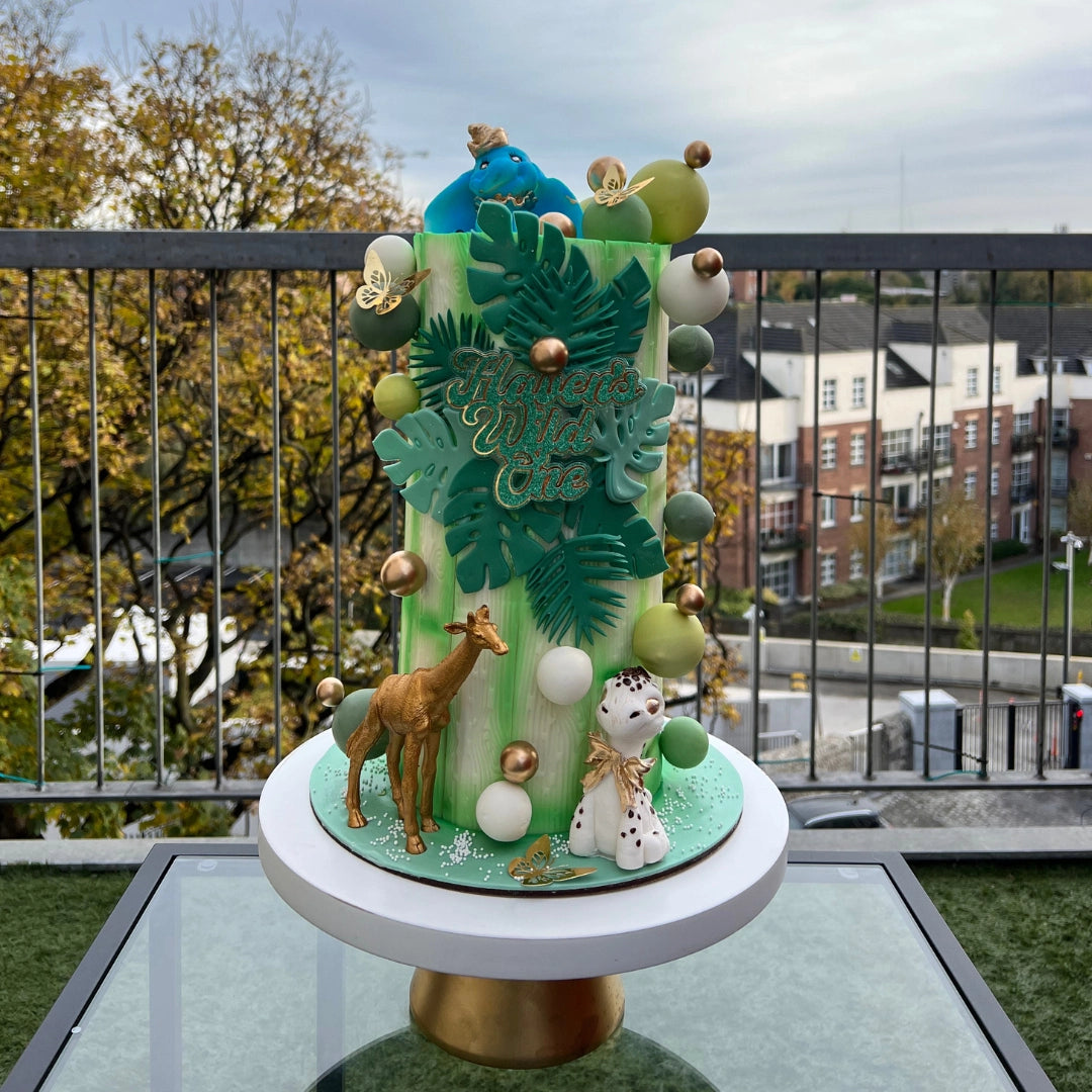 Custom-designed safari themed kids' birthday cake with green foliage and edible animal toppers.