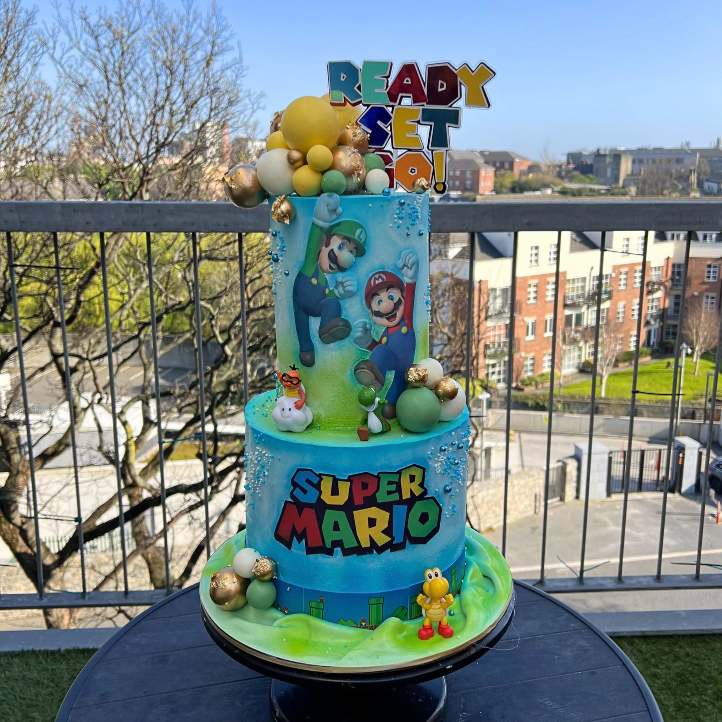 Super Mario-themed birthday cake with characters and 'Ready Set Go!' text on a balcony.