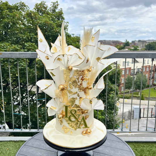 Decorative cake with gold and white Wafer paper design on a balcony with trees and buildings in the background