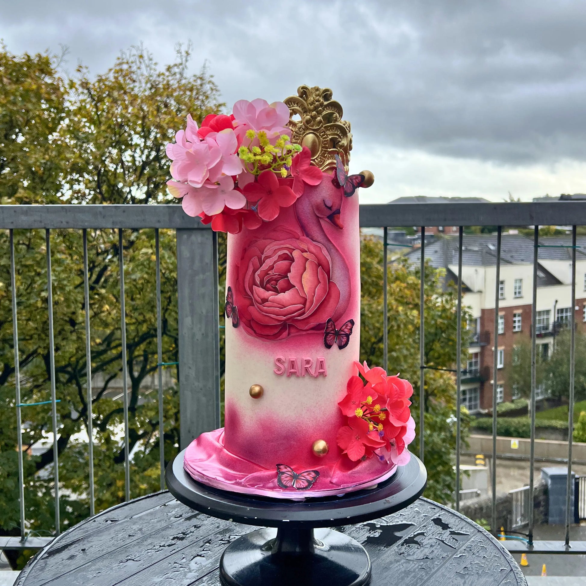 Decorative cake with pink flowers and a crown on a balcony with a cityscape background