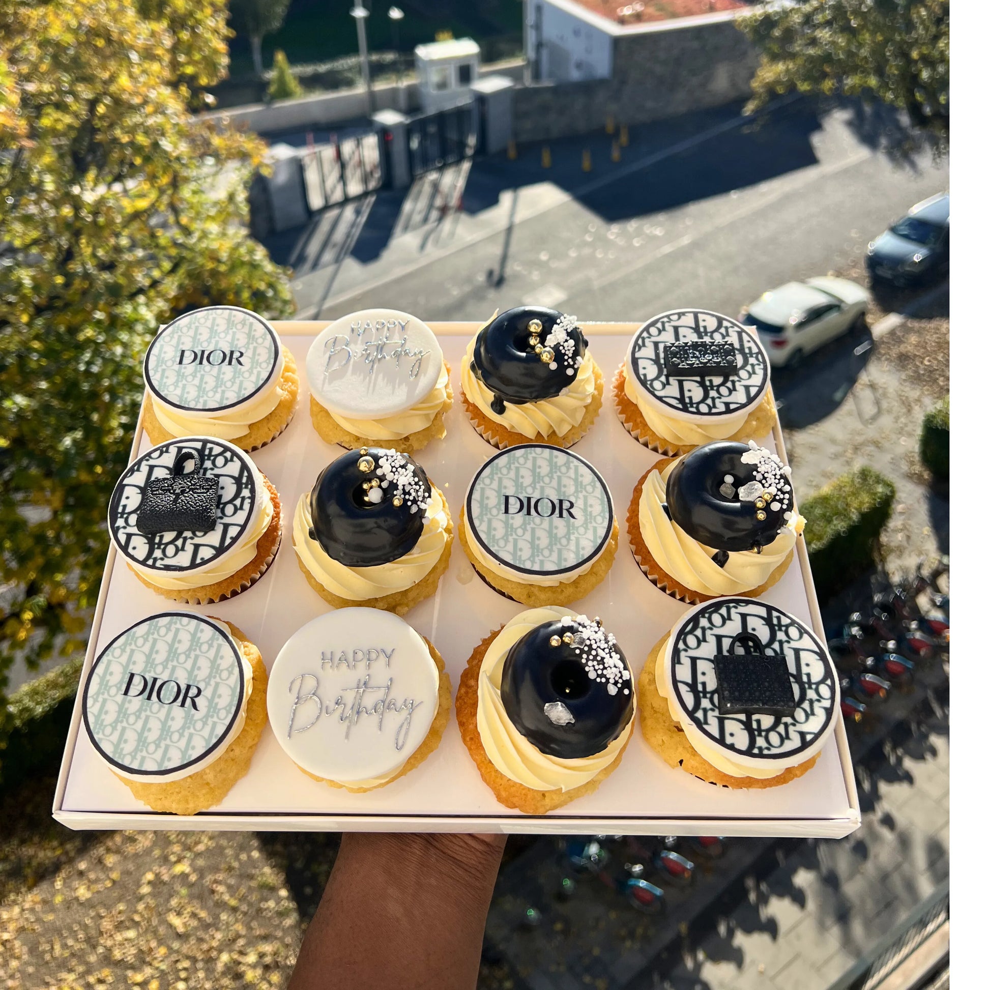 Dior-themed cupcakes on a tray with a cityscape background