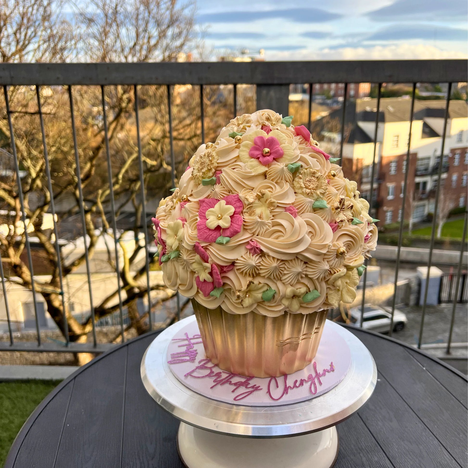 Giant cupcake cake with floral details on a stand outdoors.