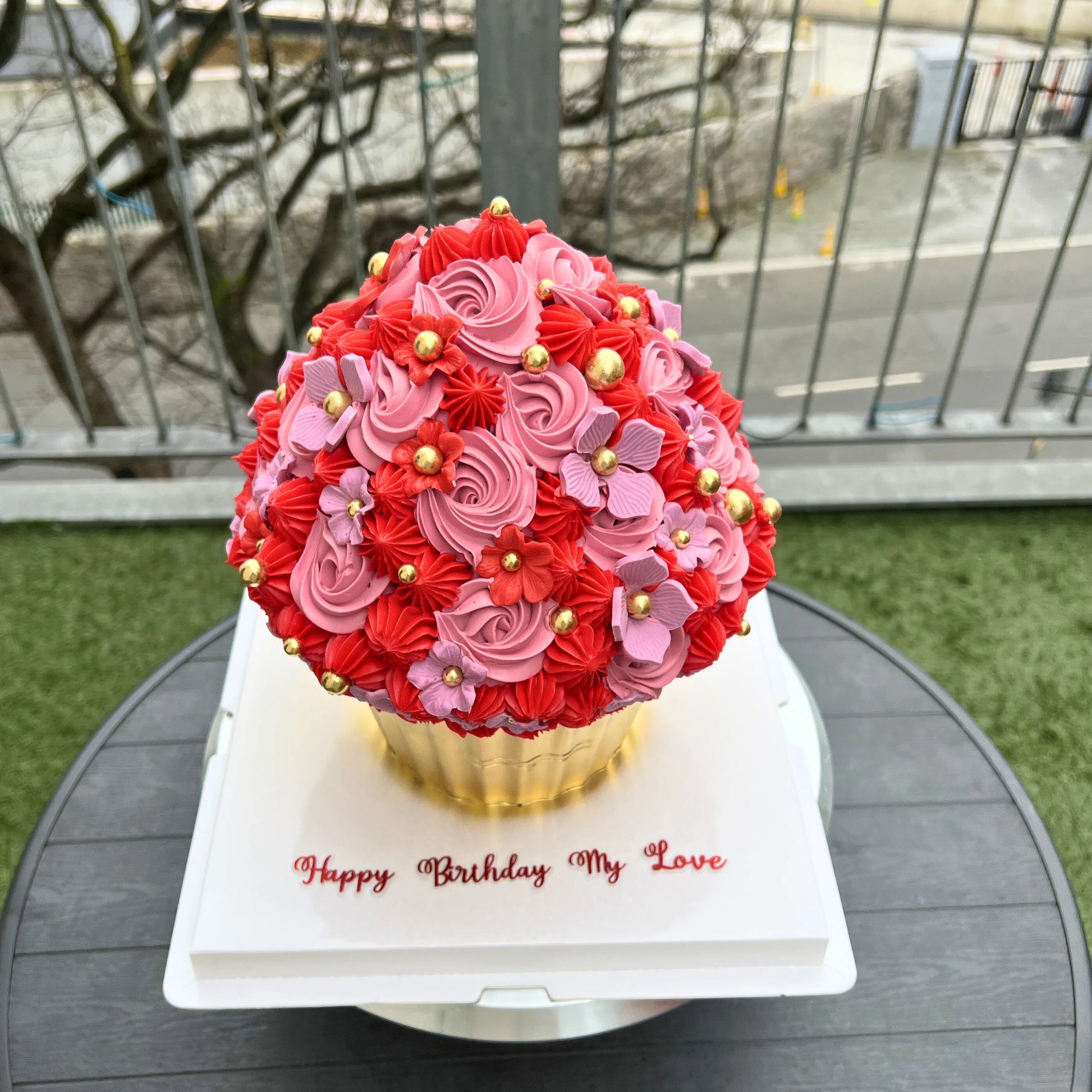 Decorative cupcake with red and pink flowers on a white stand outdoors.