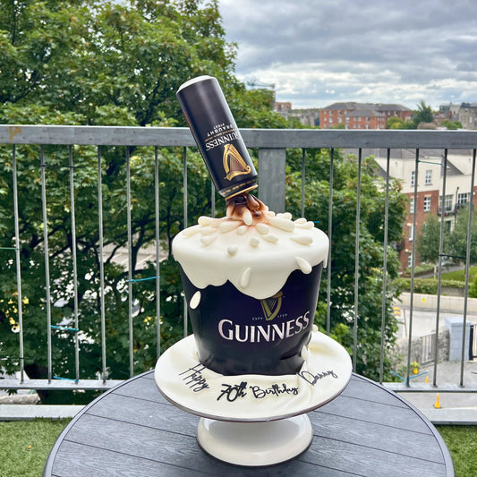 Guinness-themed birthday cake with a Guinness can on top, outdoors.