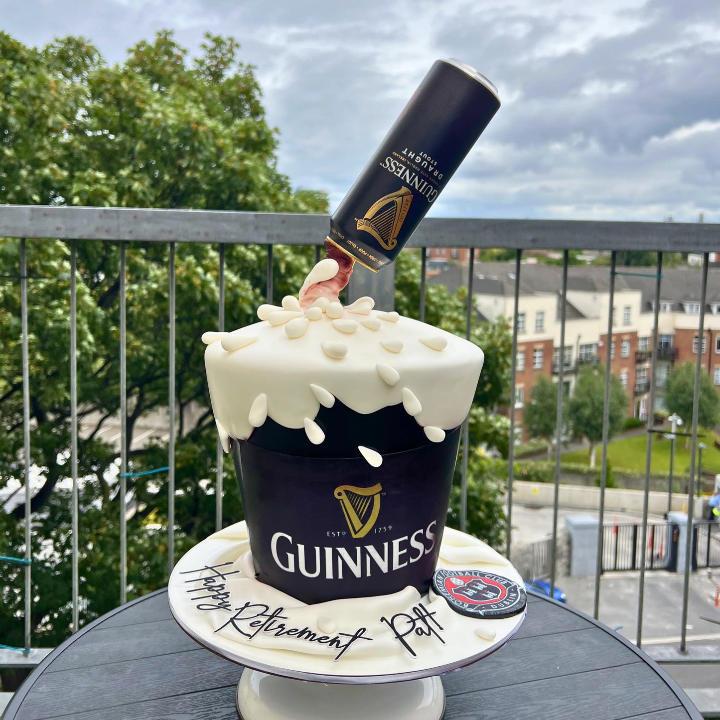 Guinness-themed cake with a bottle on top, placed outdoors.