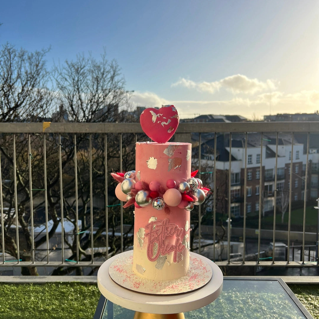 A decorated cake with pink buttercream and a heart-shaped toping.