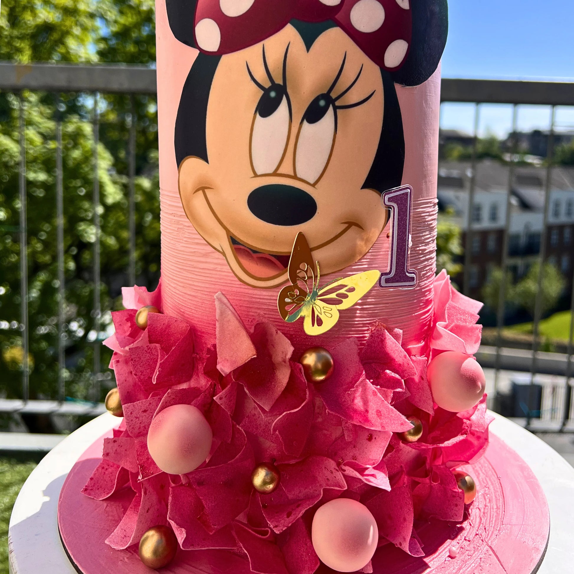 Pink birthday cake with Minnie Mouse face and decorations outdoors