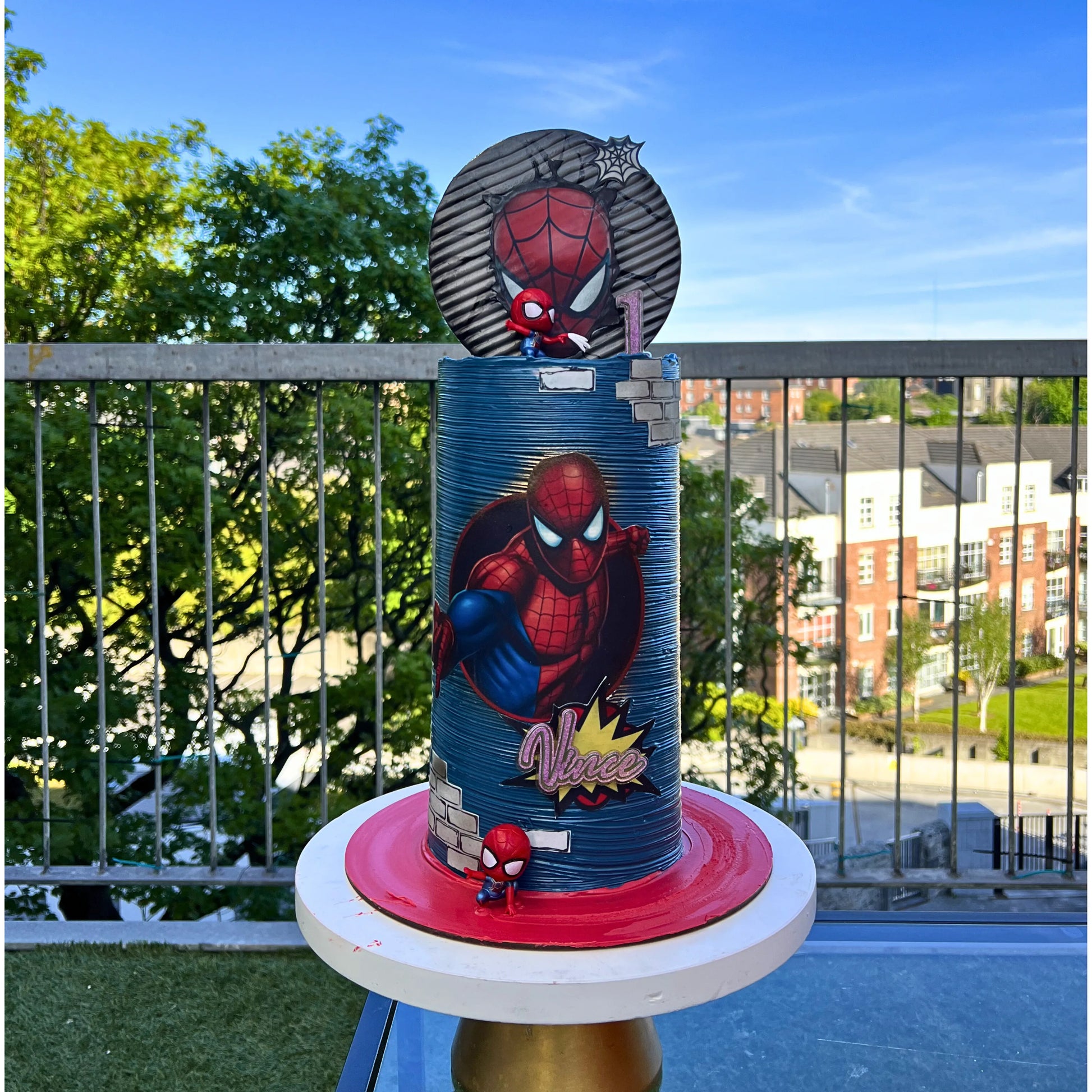 Spider-Man themed birthday cake on a balcony with trees and buildings in the background