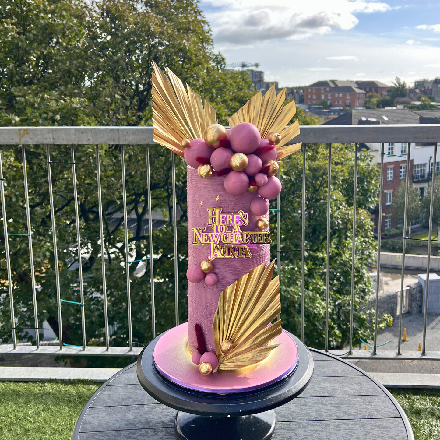 Decorative lilac and gold cake on a stand with a cityscape background