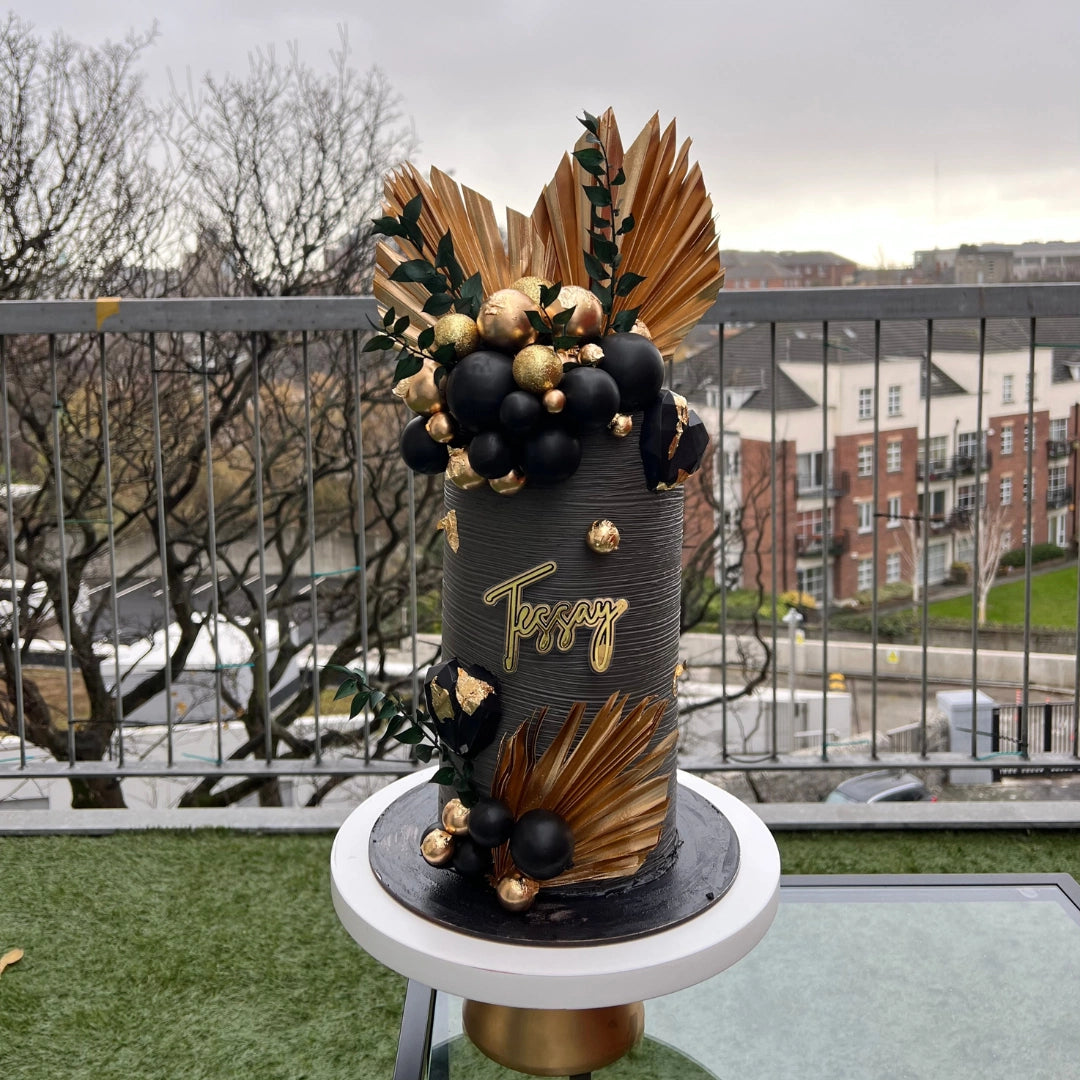 Tall luxury black buttercream cake with hand-painted gold leaf accents and artistic floral textures, bespoke design by CakeMeAway Dublin.