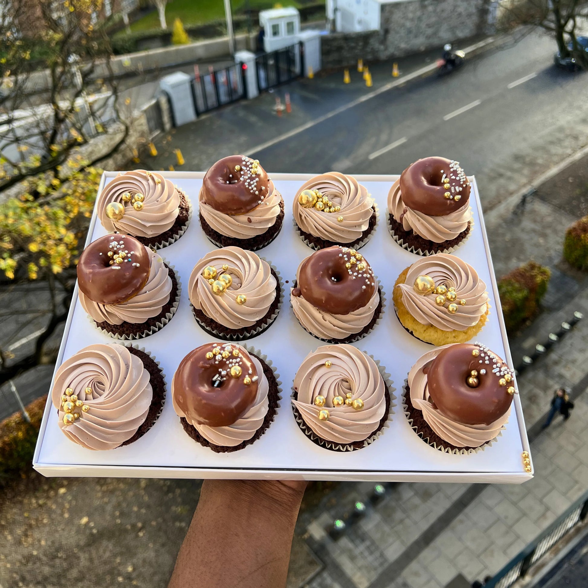 Tray of cupcakes with chocolate and vanilla frosting held above a street scene.