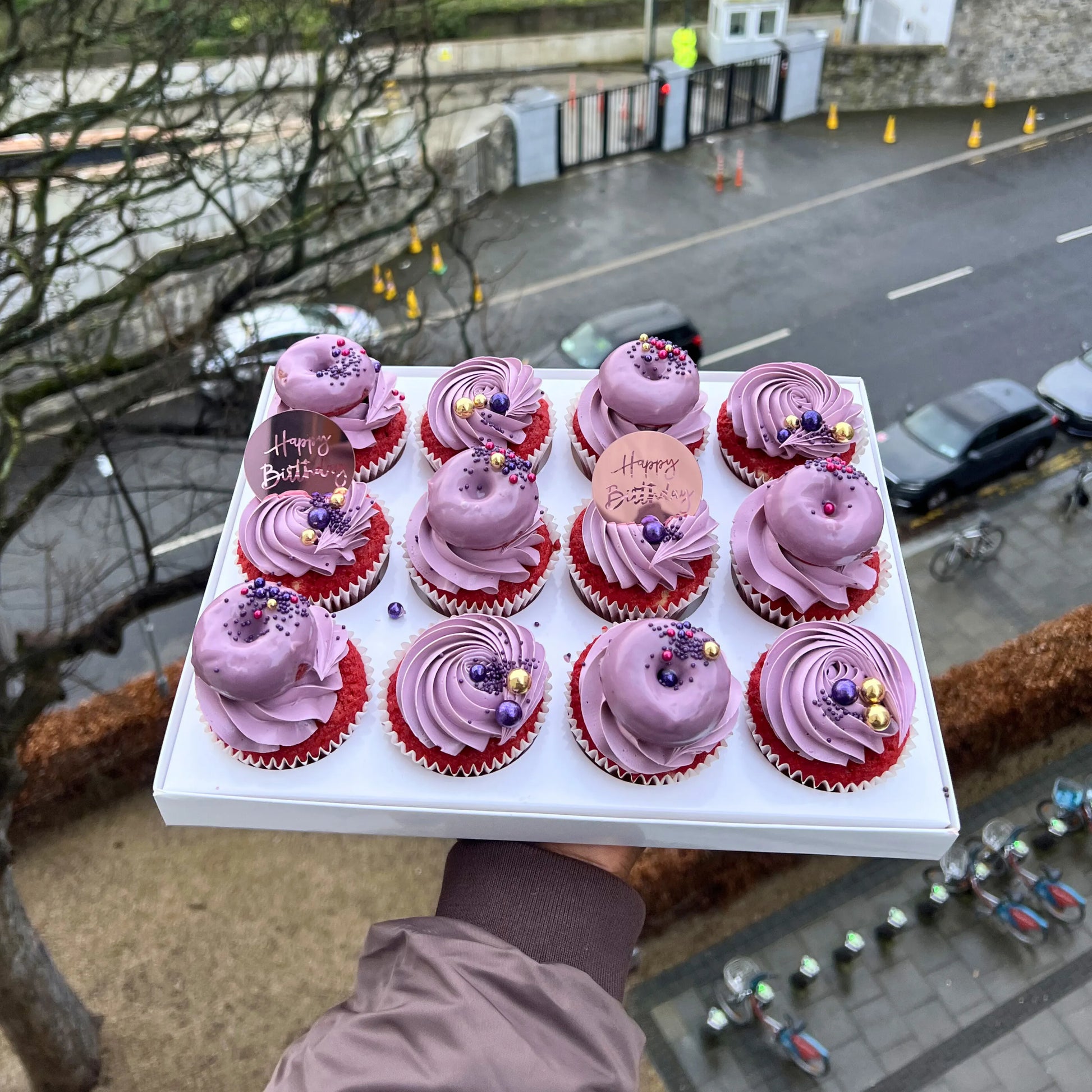 Tray of pink cupcakes with red bases held above a street scene