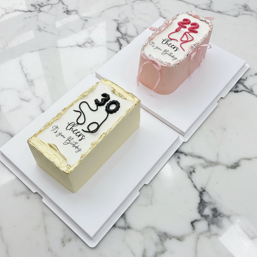 Two cakes on a white stand with decorative text and designs.