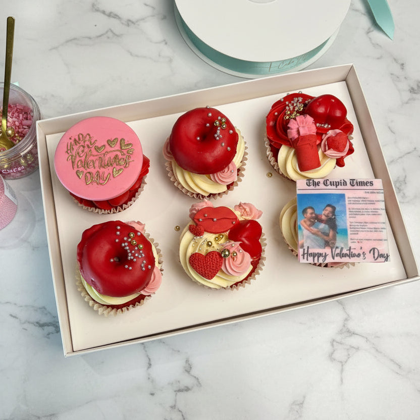 Box of Valentine's Day-themed cupcakes and donuts with a magazine on a marble surface