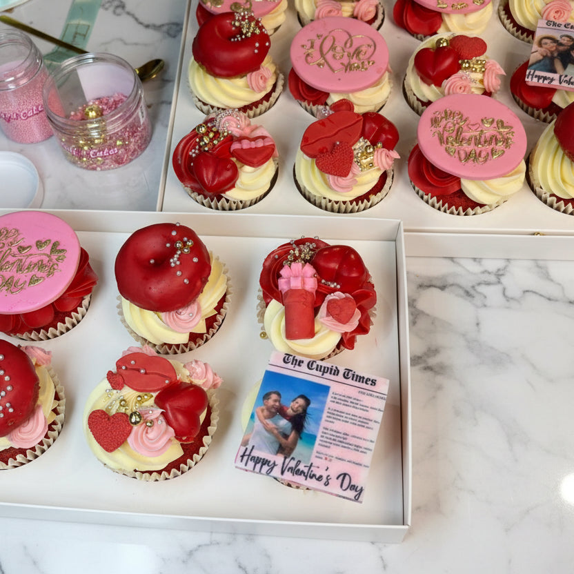 Valentine's Day-themed cupcakes with red, pink, and gold decorations in a box.