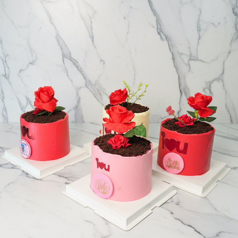 Four small cakes designed to look like potted plants with red roses on a marble background