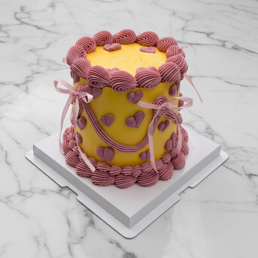 Yellow cake with pink decorative love pipping elements 
