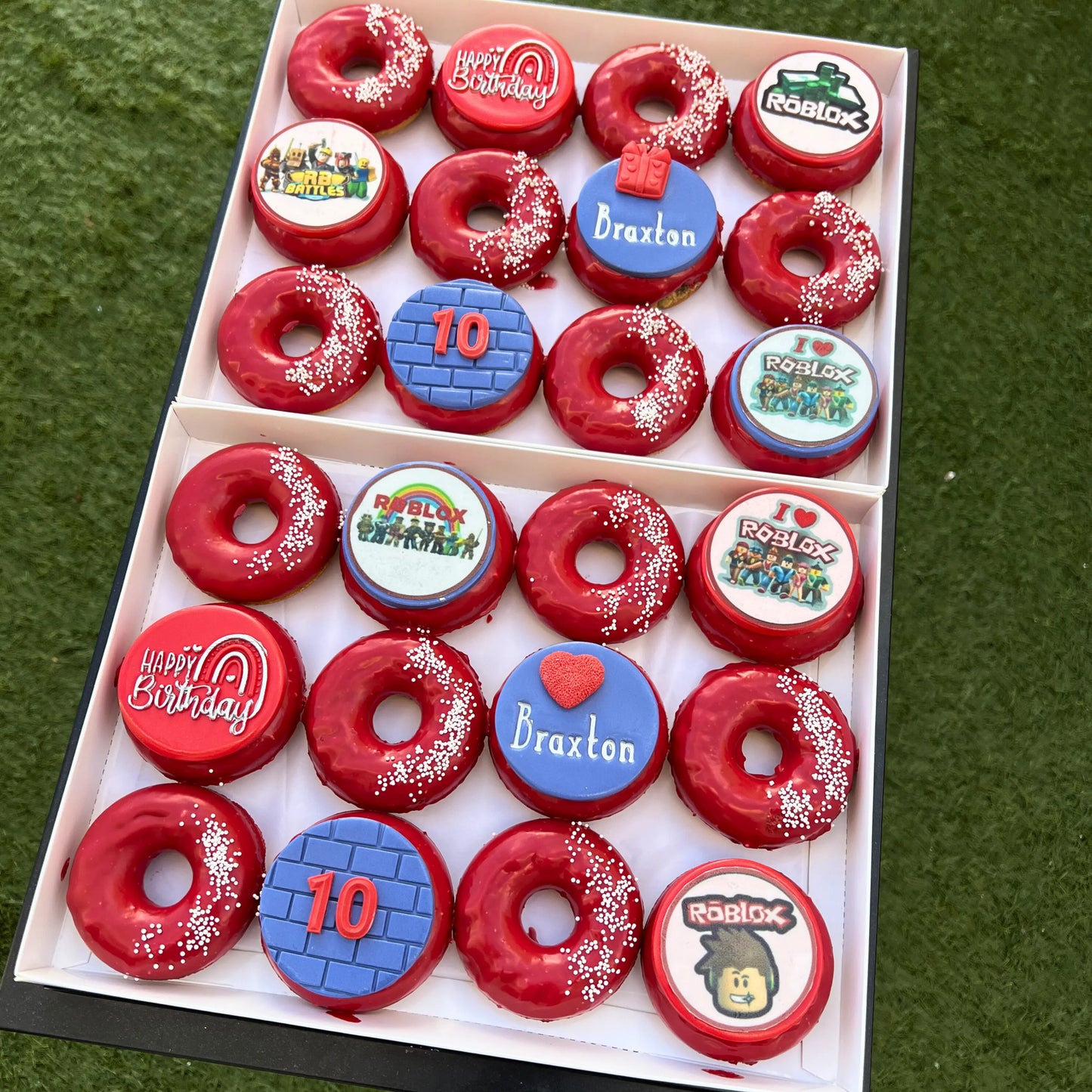 2 Boxes of red donuts with personalized roblox theme toppers on a green grass background