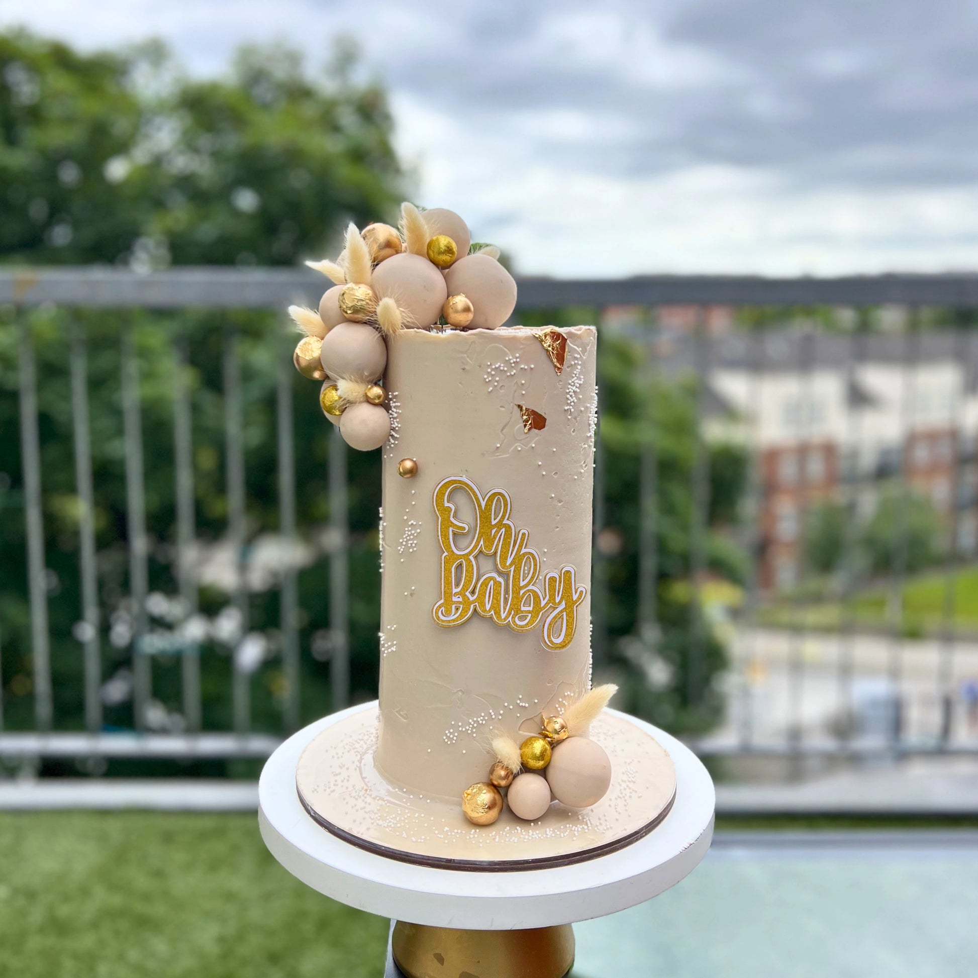 Baby shower cake with 'Oh Baby' text and decorative elements on a stand outdoors.
