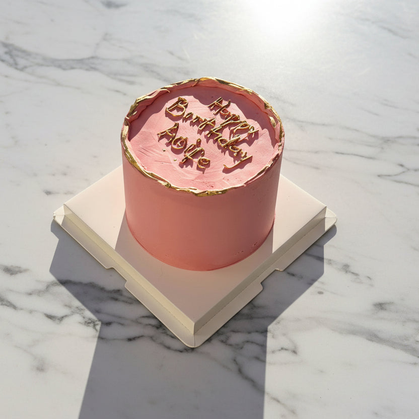 Pink cake with gold rim on a white platform outdoors
