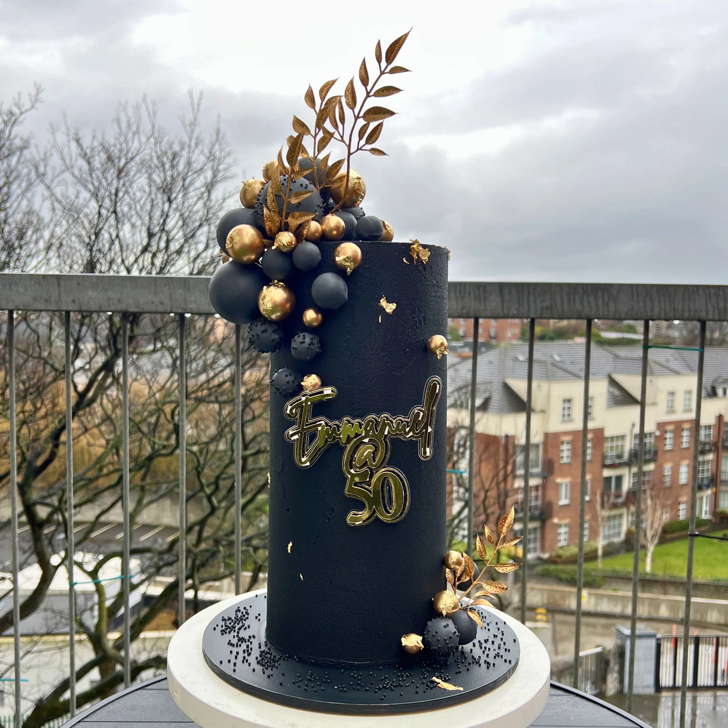 Decorative cake with gold and black elements on a balcony with a cityscape background