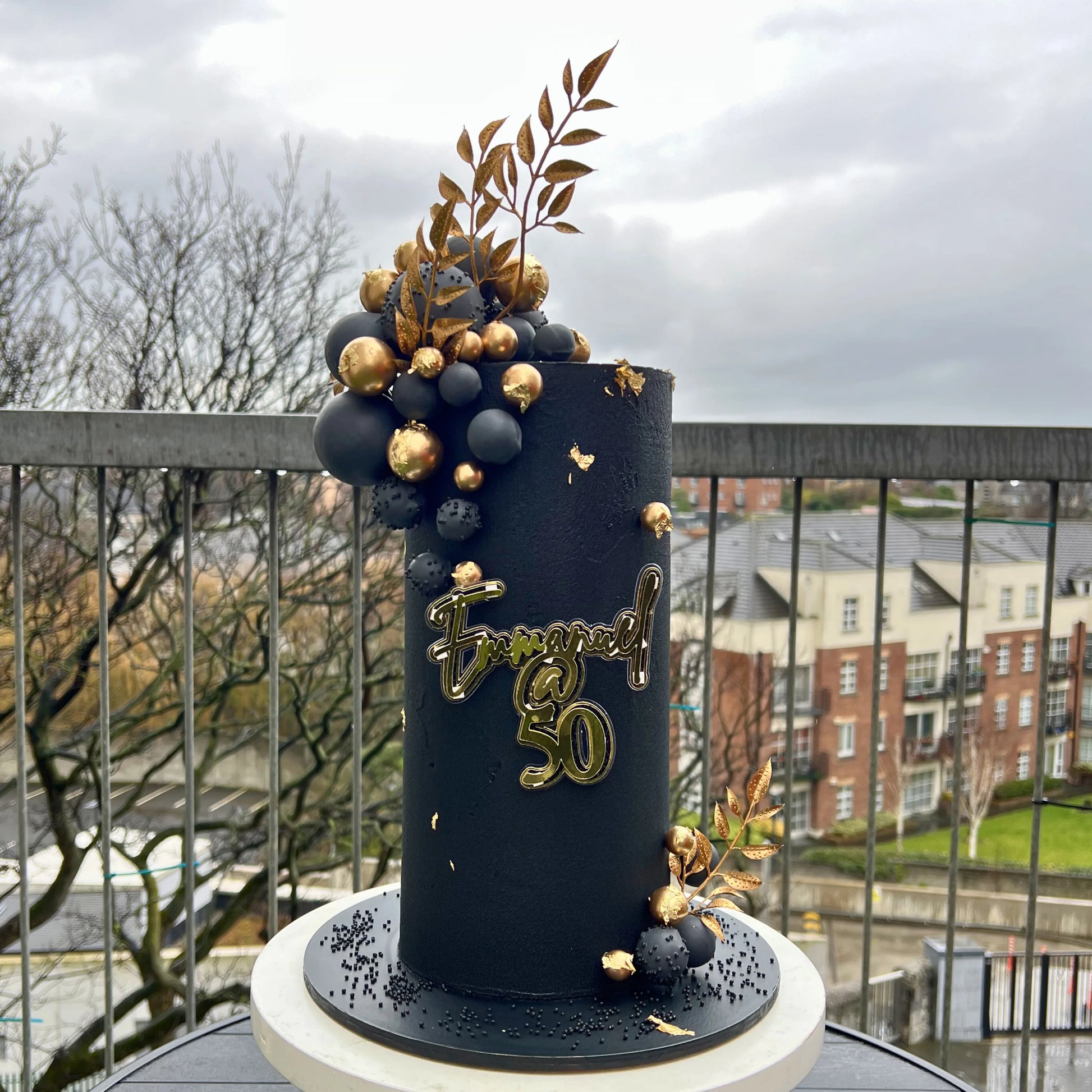Decorative cake with gold and black elements on a balcony with a cityscape background