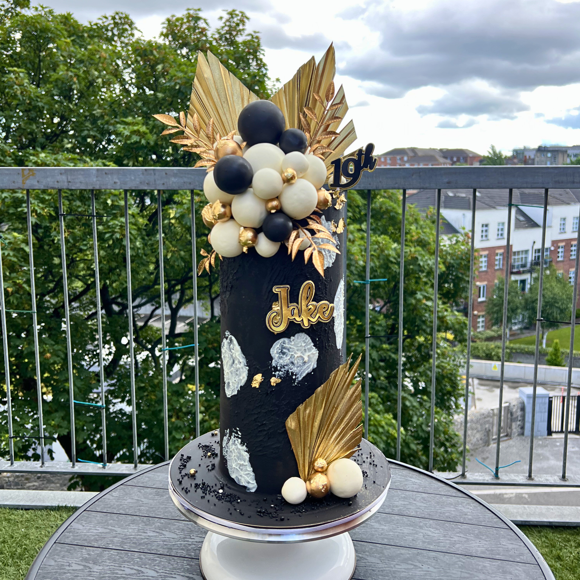 ivory cake with gold and black design with palm spears on a table outdoors